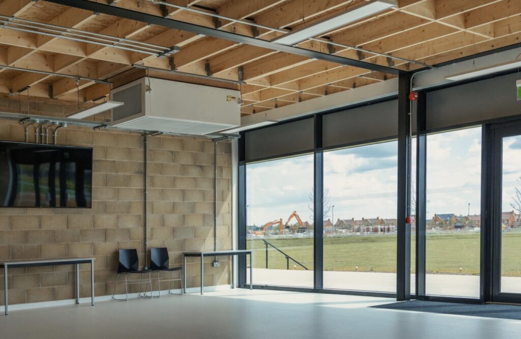 Image shows the main hall at the pavilion which is used for classes. It shows a room with walls on three sides with glass patio doors on the fourth allowing for lots of natural light to enter the room. The floor is smooth and flat and there is also a high ceiling.